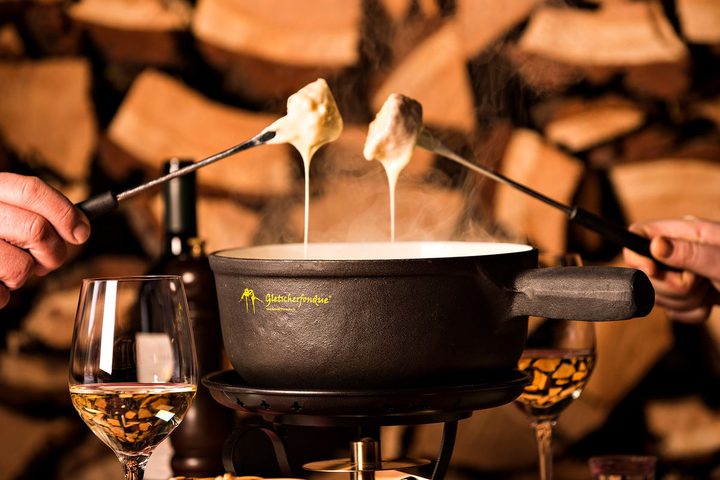 Käsefondue im Gletscherfondue-Caquelon, zwei Gabeln mit fließendem Käse